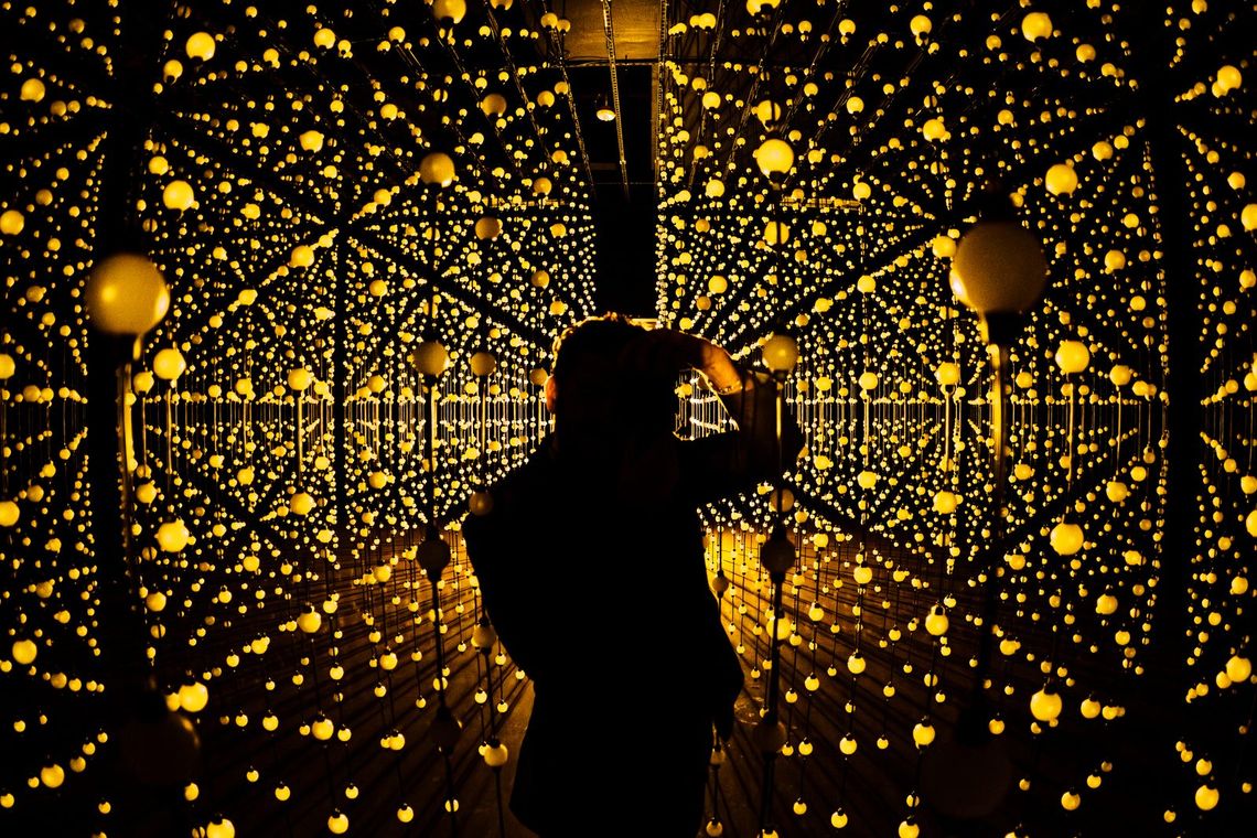 A guest photographing the endless grid of bulbs in Unknown Atmospheres, Portland, everything glowing gold.