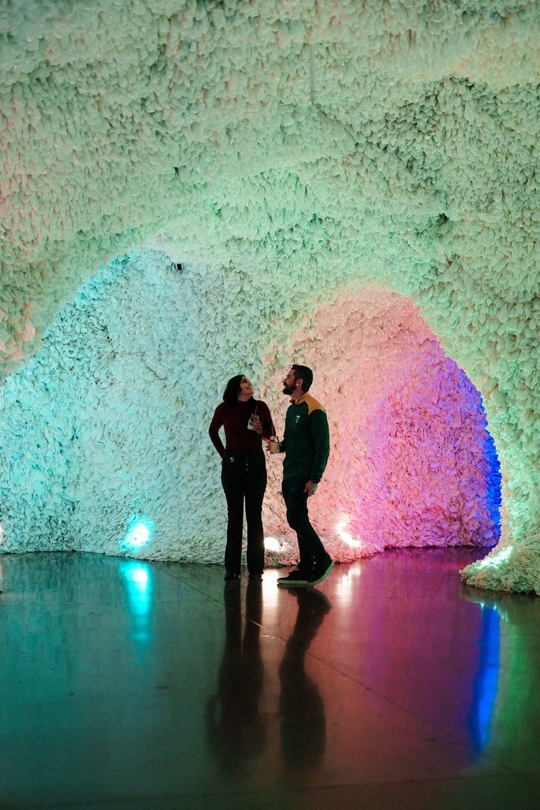 Two guests stand talking under a glowing arch in Rainbow Cave, their reflections on the shiny floor.