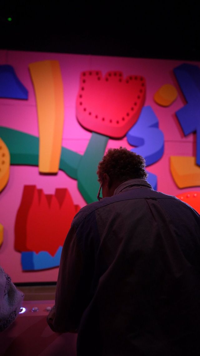 A guest at the console looks up at the pink wall of painted flowers and shapes in Are You There?