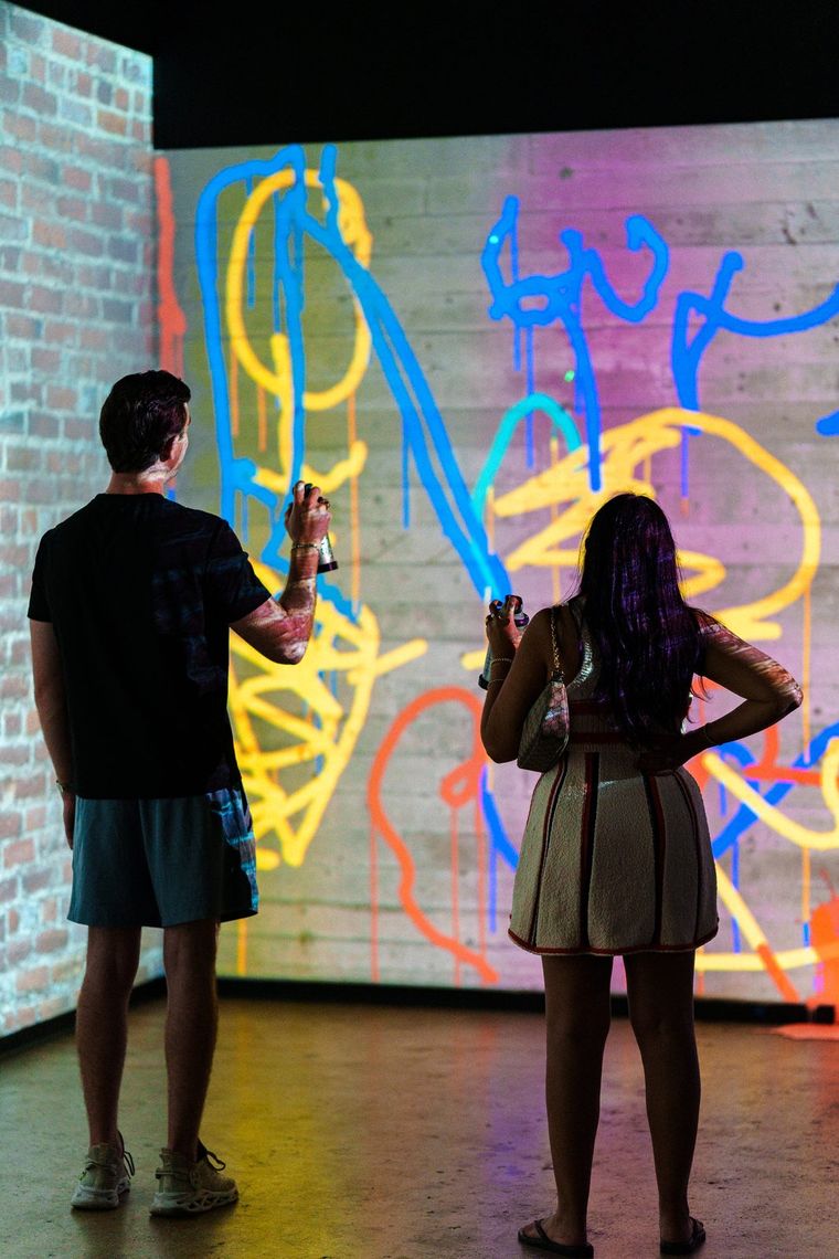 Two guests with laser spray cans in Laser Graffiti, blue, yellow and orange scribbles dripping down the projected wall.